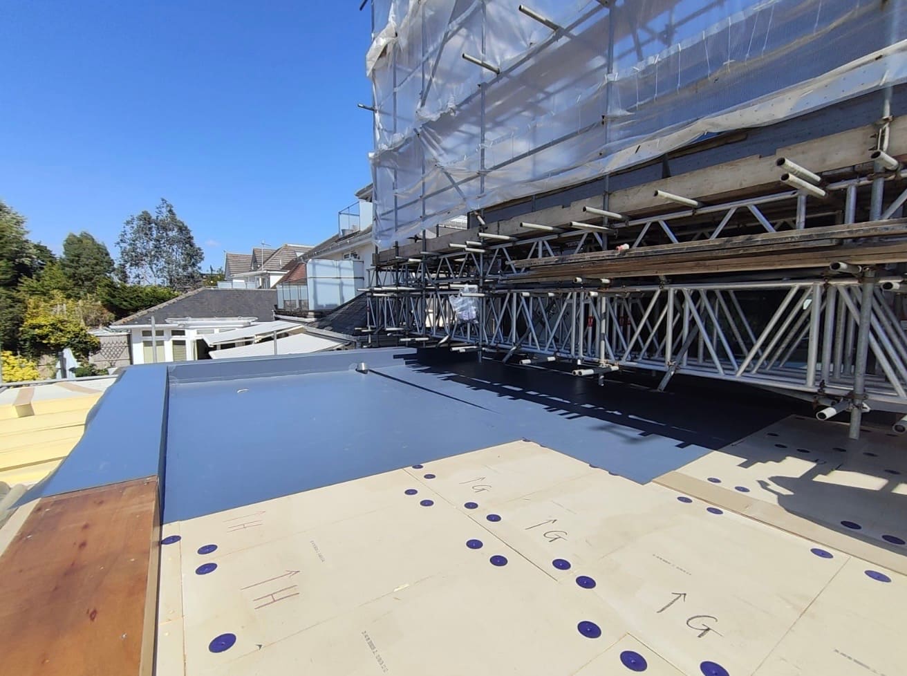 Insulation boards being fixed across a large roof deck under scaffolding
